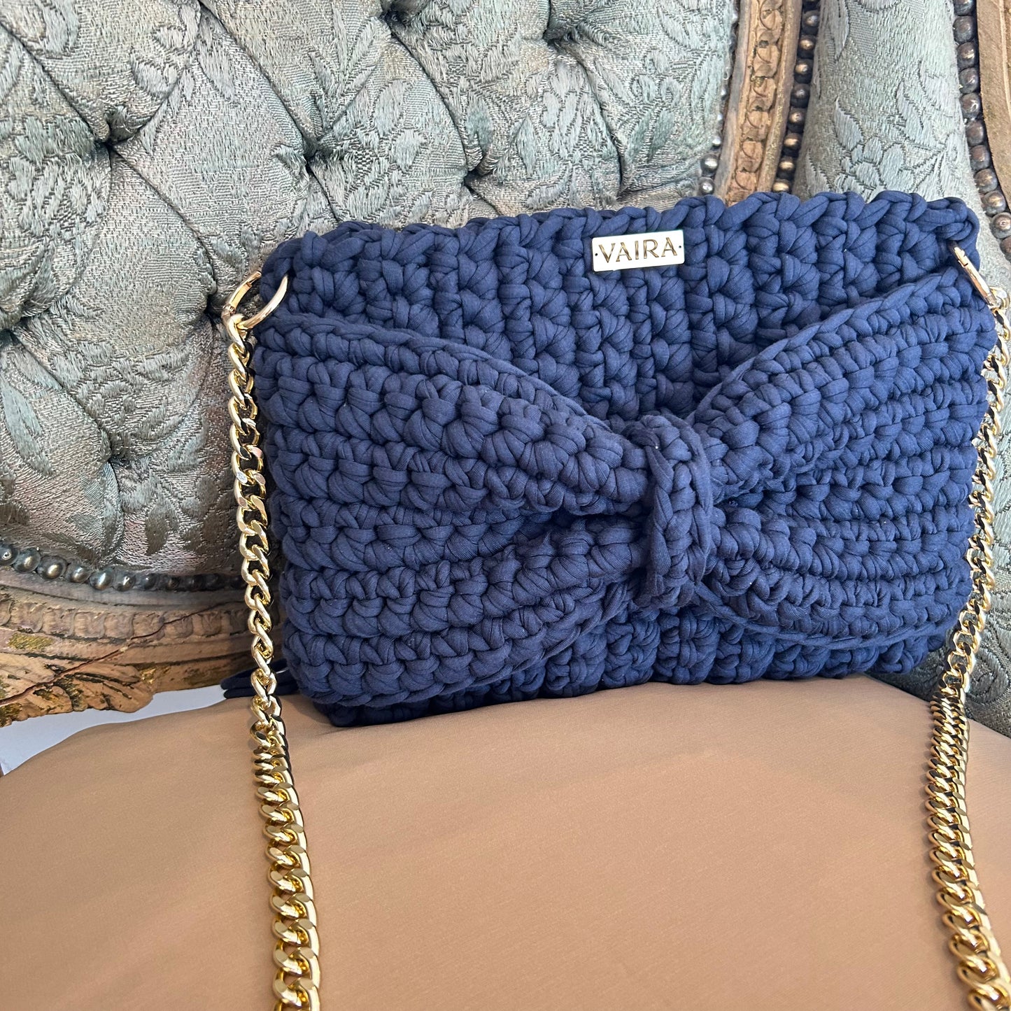 Handcrafted crochet shoulder bag featuring a 3D bow detail, soft fringe accents, and a gold chain strap. Elegant and boho-inspired, with a textured weave and spacious design—perfect for day-to-night styling.