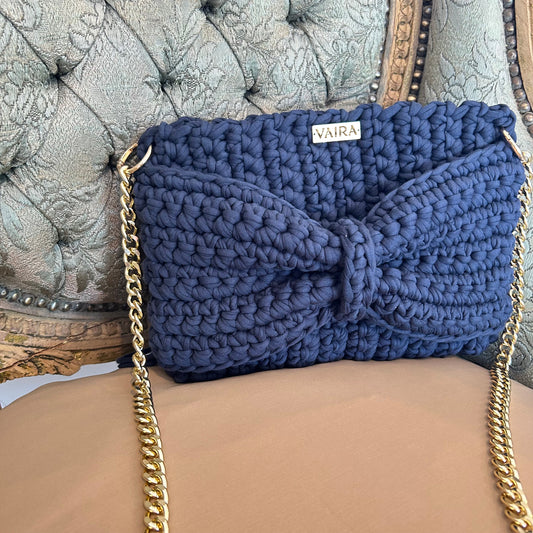 Handcrafted crochet shoulder bag featuring a 3D bow detail, soft fringe accents, and a gold chain strap. Elegant and boho-inspired, with a textured weave and spacious design—perfect for day-to-night styling.